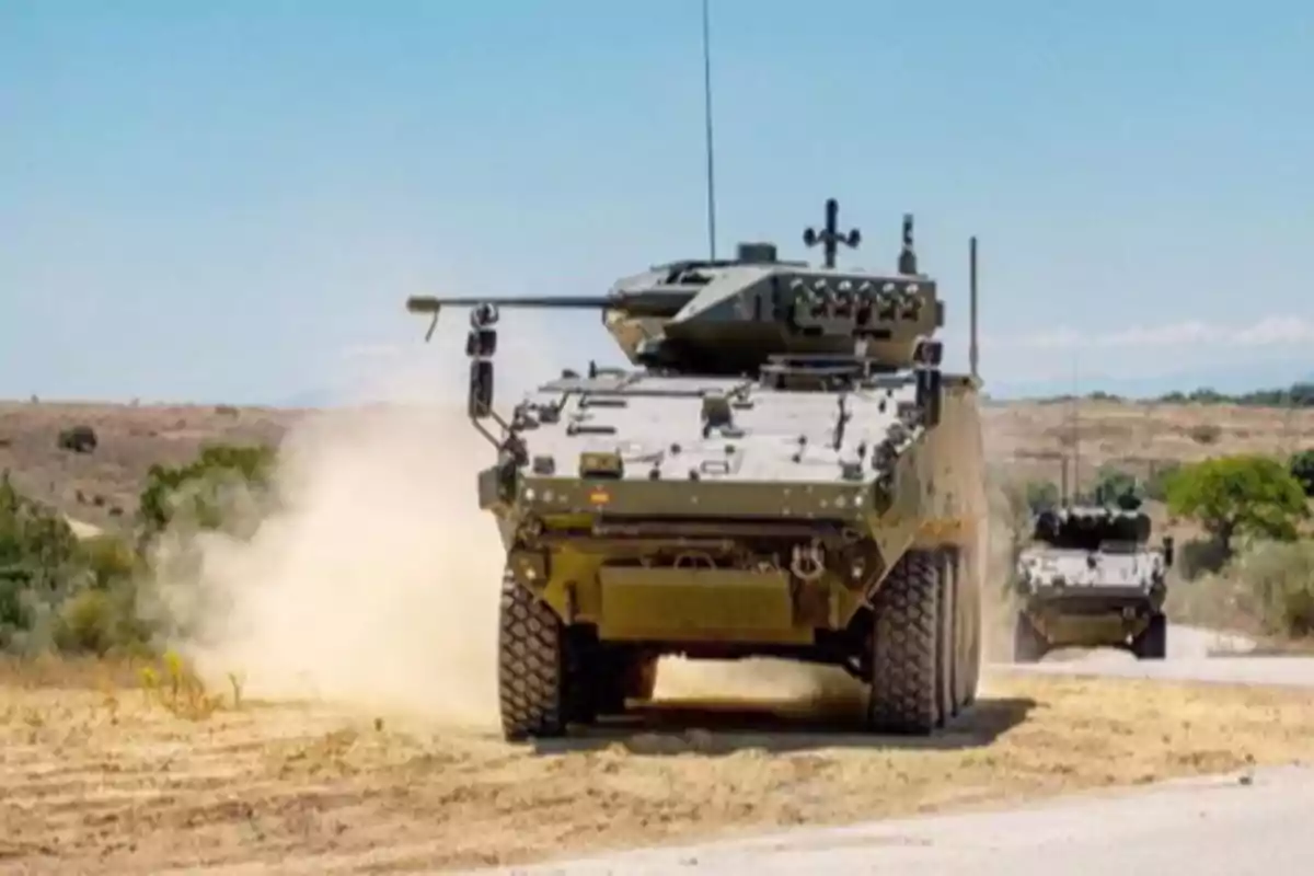 Vehículo blindado militar avanzando por un camino polvoriento en un entorno rural.