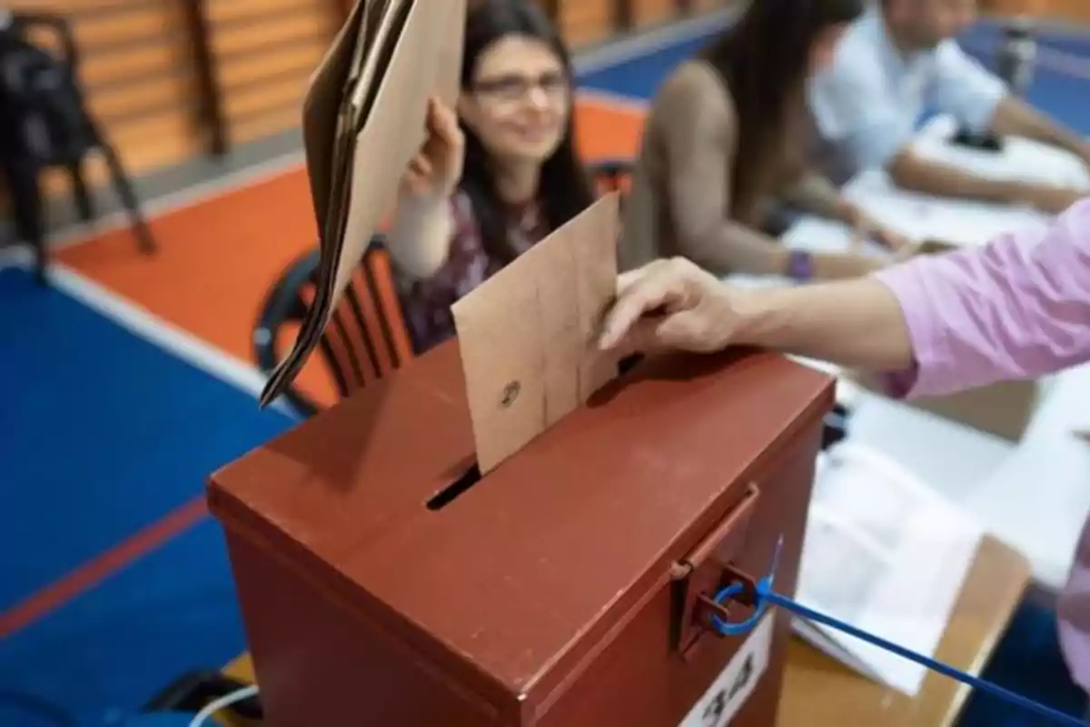 Persona depositando un sobre en una urna de votación en un centro electoral.