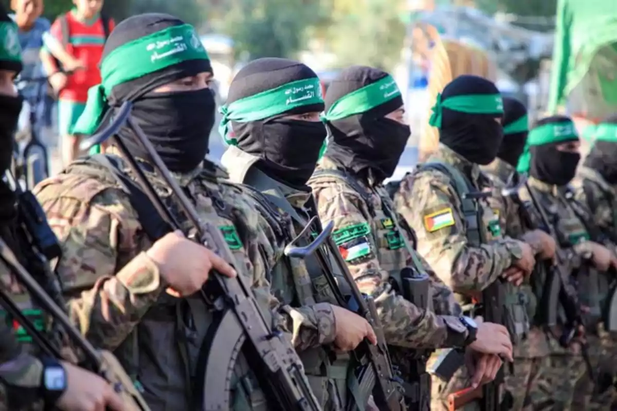 Un grupo de personas vestidas con uniformes de camuflaje y pañuelos verdes en la cabeza, sosteniendo armas y alineadas en formación. Un grupo de personas vestidas con uniformes de camuflaje y pañuelos verdes en la cabeza, sosteniendo armas y alineadas en formación.
