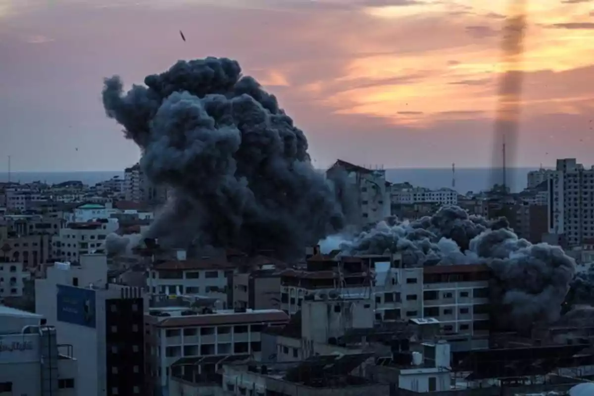 Una gran nube de humo negro se eleva sobre una ciudad al atardecer tras una explosión. Una gran nube de humo negro se eleva sobre una ciudad al atardecer tras una explosión.