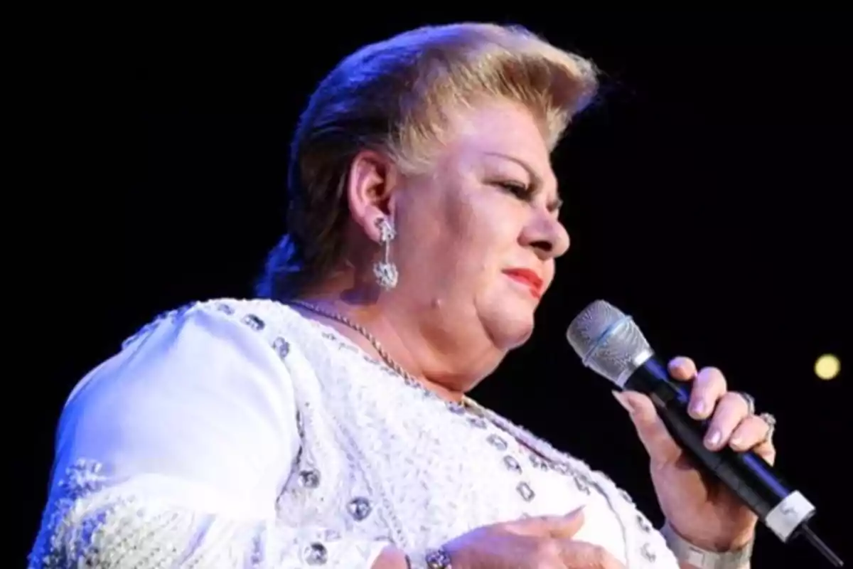 Una persona con vestido blanco decorado sostiene un micrófono mientras canta en un escenario.