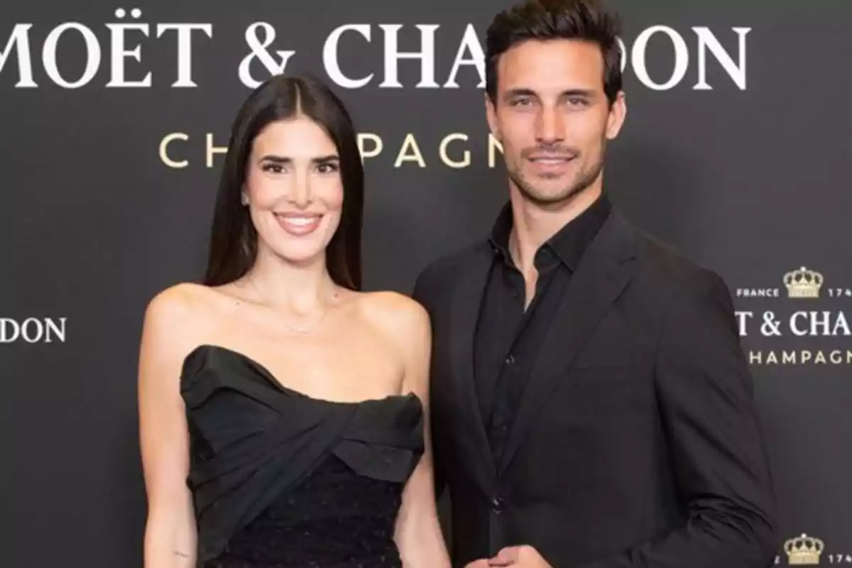 Una pareja vestida de negro posa frente a un fondo con el logo de Moët & Chandon.