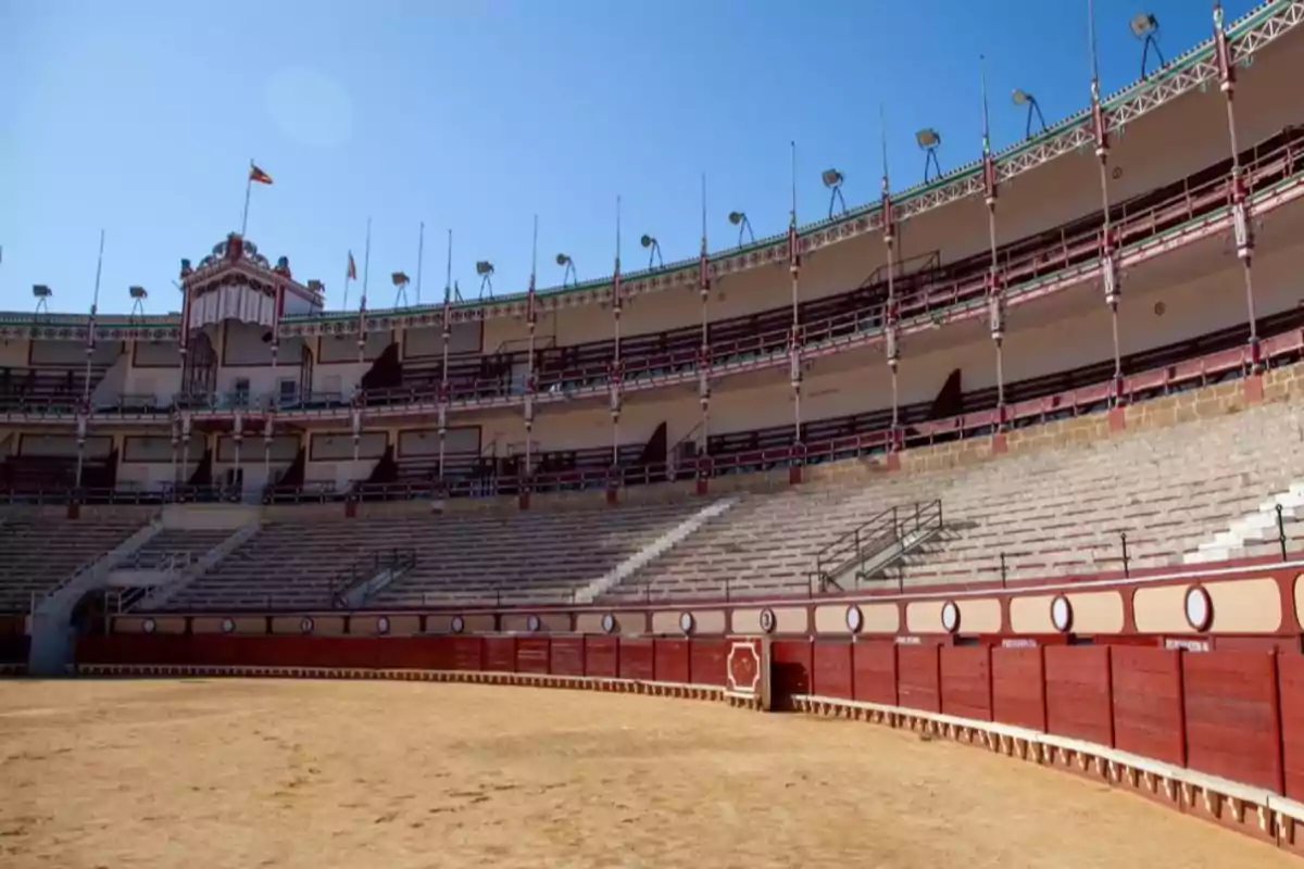 Una plaza de toros vacía con gradas y barreras de madera bajo un cielo despejado.