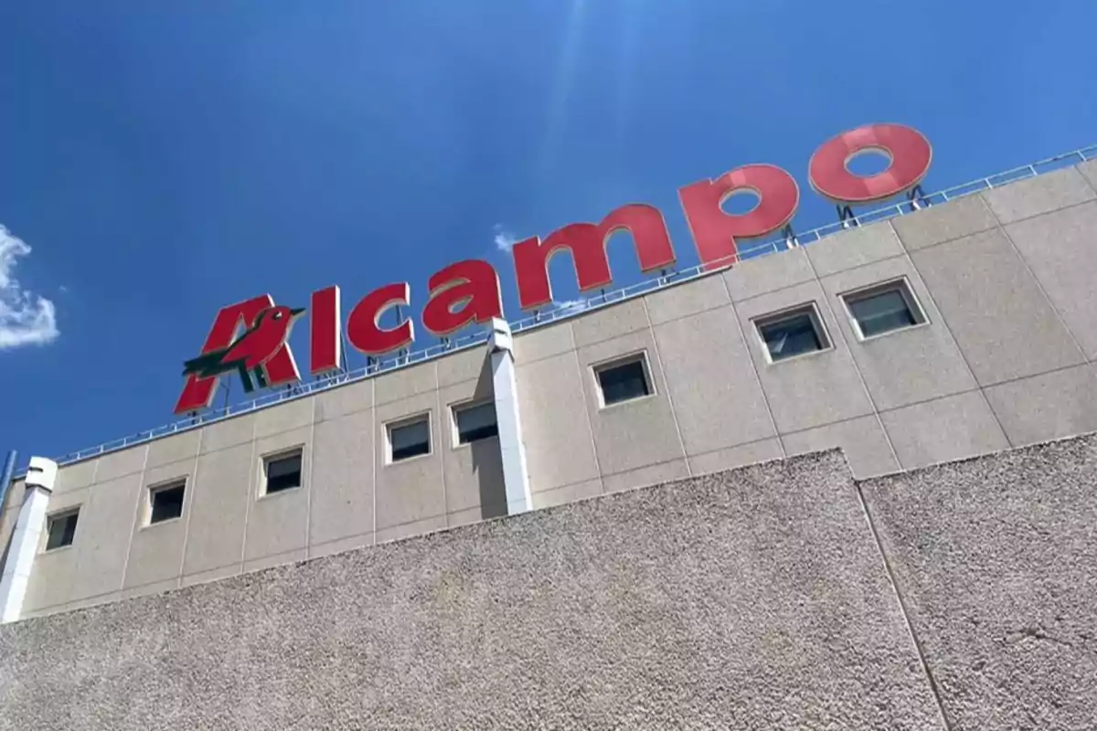Edificio con el logotipo de Alcampo en letras rojas sobre un fondo de cielo azul. Edificio con el logotipo de Alcampo en letras rojas sobre un fondo de cielo azul.