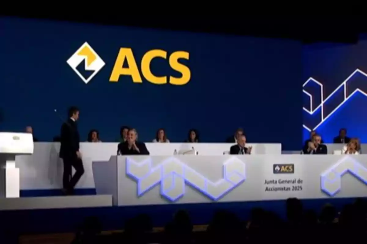 Personas sentadas en una mesa principal durante la Junta General de Accionistas 2025 de ACS, con el logotipo de la empresa en grande al fondo. Personas sentadas en una mesa principal durante la Junta General de Accionistas 2025 de ACS, con el logotipo de la empresa en grande al fondo.