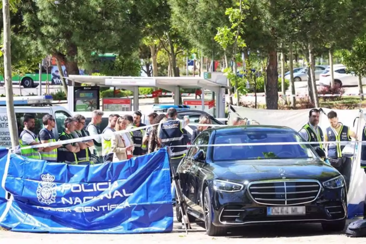 Un grupo de personas con chalecos de la Policía Nacional se encuentra en una escena acordonada con un coche negro y una furgoneta de la policía en un entorno arbolado. Un grupo de personas con chalecos de la Policía Nacional se encuentra en una escena acordonada con un coche negro y una furgoneta de la policía en un entorno arbolado.