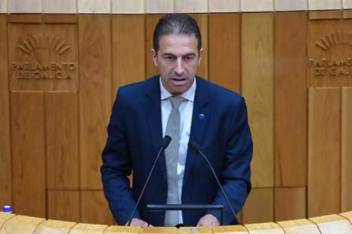 Hombre con traje oscuro hablando en un atril en el Parlamento de Galicia Hombre con traje oscuro hablando en un atril en el Parlamento de Galicia