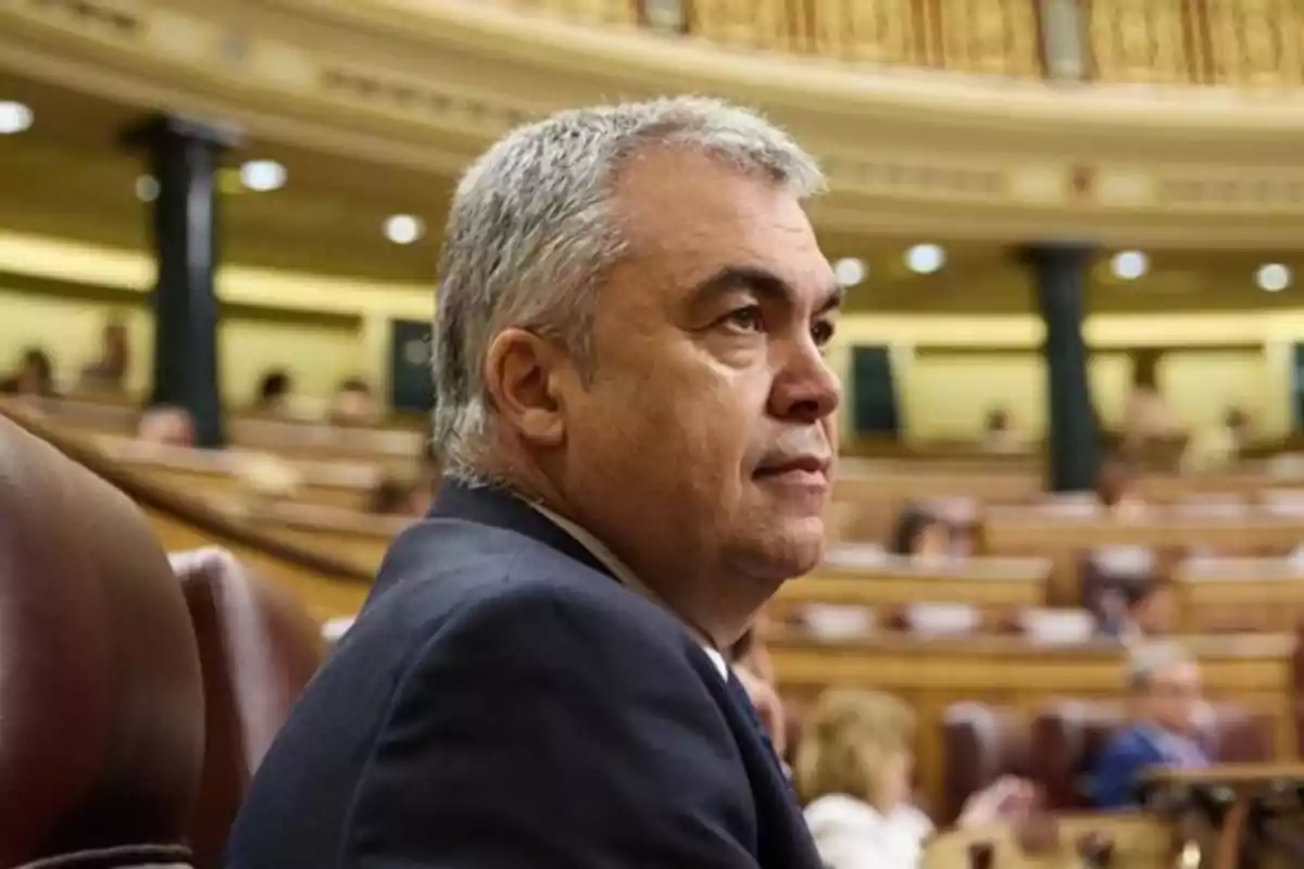 Hombre de cabello canoso sentado en un recinto parlamentario con expresión seria Hombre de cabello canoso sentado en un recinto parlamentario con expresión seria