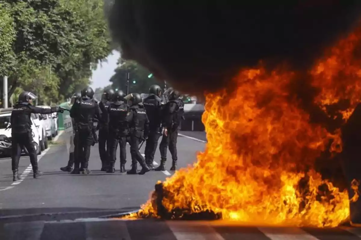 Policías antidisturbios en una calle frente a una gran llamarada y humo negro durante una protesta