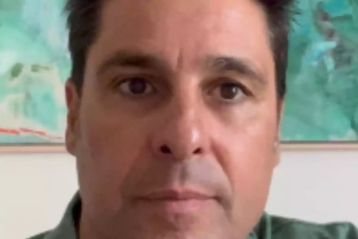 Un hombre con cabello oscuro y expresión neutral frente a un fondo verde. Un hombre con cabello oscuro y expresión neutral frente a un fondo verde.