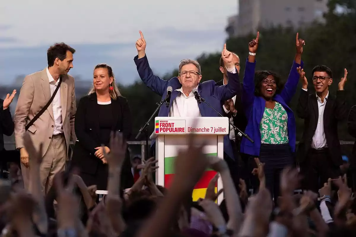 Un grupo de personas en un mitin político con un orador principal levantando los brazos en señal de victoria.