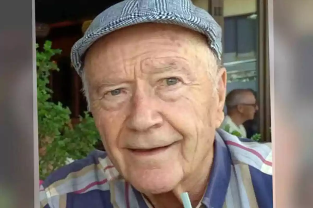 Un hombre mayor con una gorra a cuadros y una camisa de rayas sonríe mientras está sentado en un lugar al aire libre.