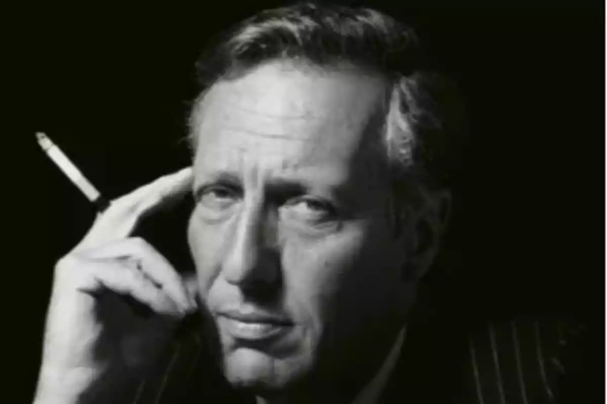 Hombre de mediana edad en blanco y negro sosteniendo un cigarro junto a su rostro con expresión seria Hombre de mediana edad en blanco y negro sosteniendo un cigarro junto a su rostro con expresión seria