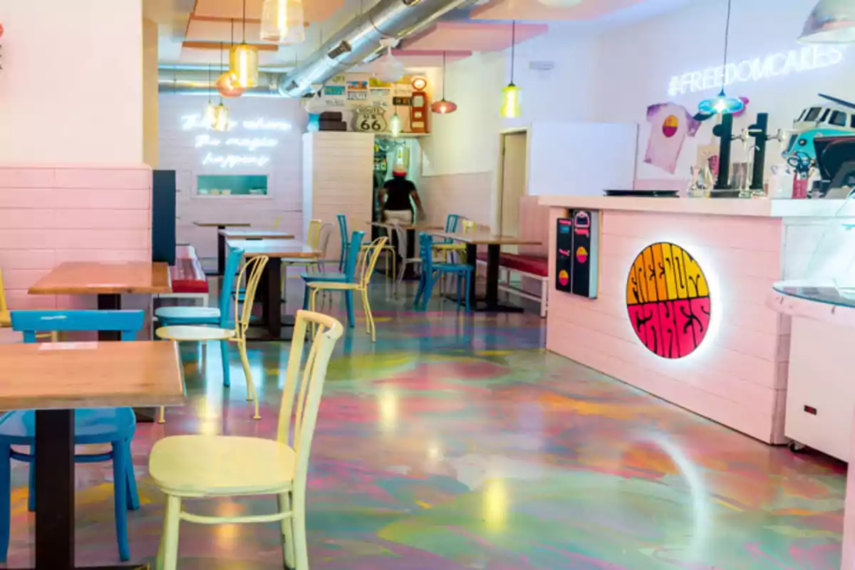 Una cafetería con decoración colorida, sillas de diferentes colores, un suelo con diseño psicodélico y luces de neón.