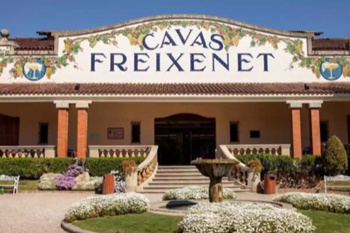 Entrada principal de una bodega con un letrero que dice "Cavas Freixenet" rodeada de jardines y flores.