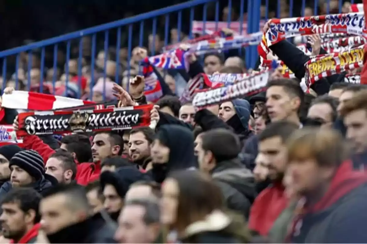 Aficionados en un estadio de fútbol sosteniendo bufandas y animando a su equipo.