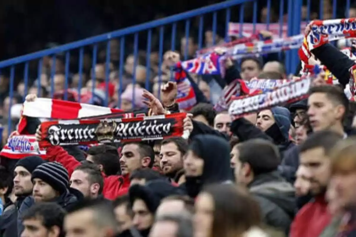 Aficionados de fútbol en las gradas sosteniendo bufandas del equipo.