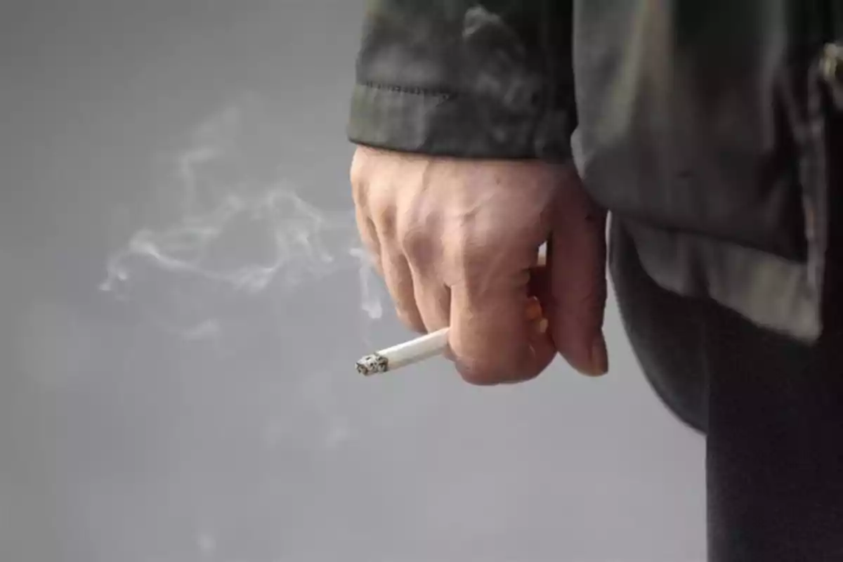 Mano sosteniendo un cigarro encendido con humo visible