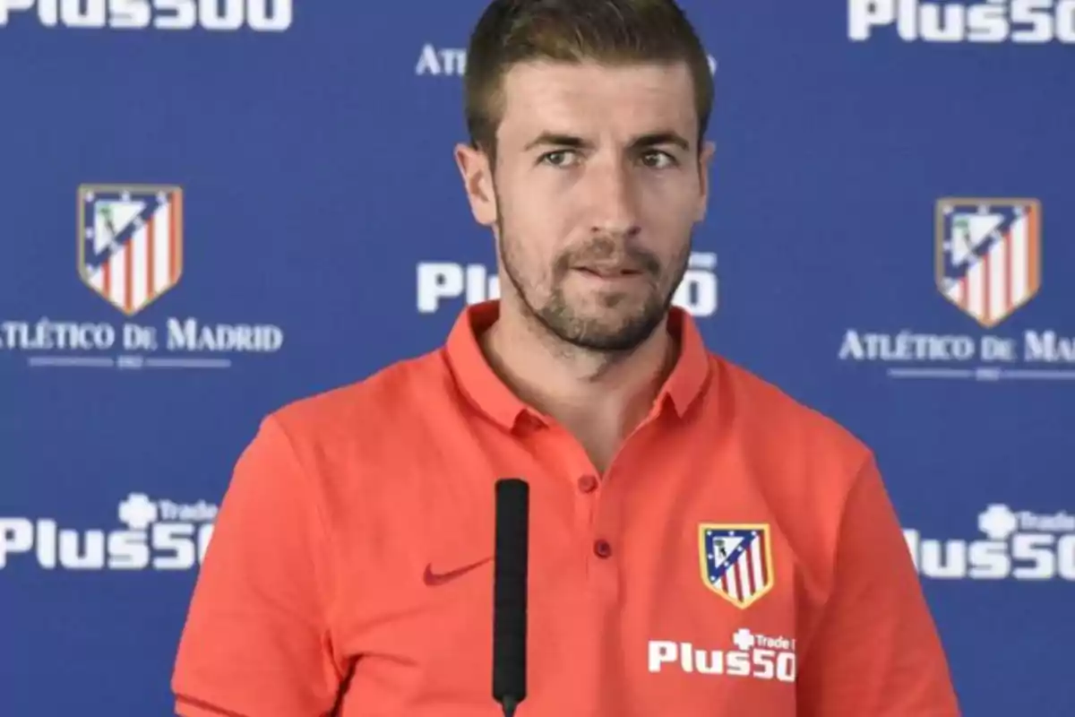 Hombre con barba corta y camisa roja del Atlético de Madrid hablando frente a un micrófono con fondo azul del club Hombre con barba corta y camisa roja del Atlético de Madrid hablando frente a un micrófono con fondo azul del club