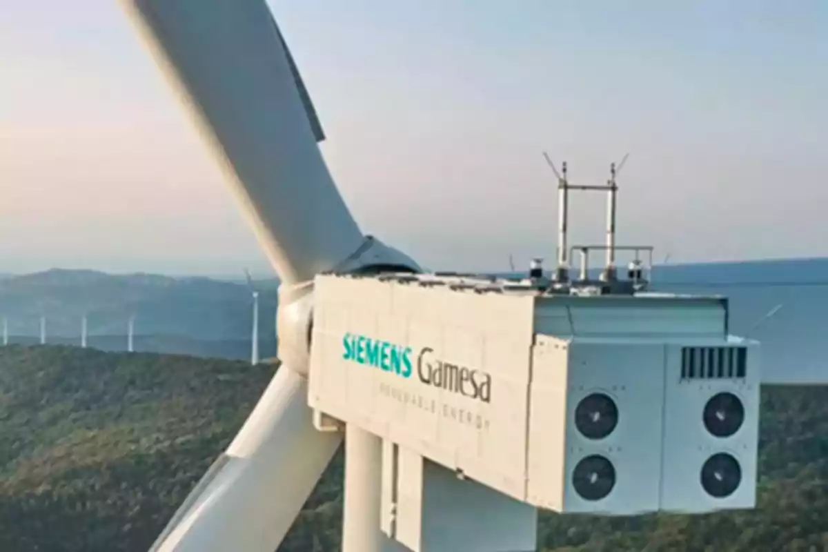 Primer plano de un aerogenerador de Siemens Gamesa con un paisaje montañoso y otros aerogeneradores al fondo. Primer plano de un aerogenerador de Siemens Gamesa con un paisaje montañoso y otros aerogeneradores al fondo.