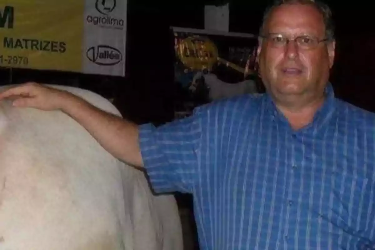 Un hombre con camisa de cuadros azules posa junto a una vaca blanca en un evento agrícola.