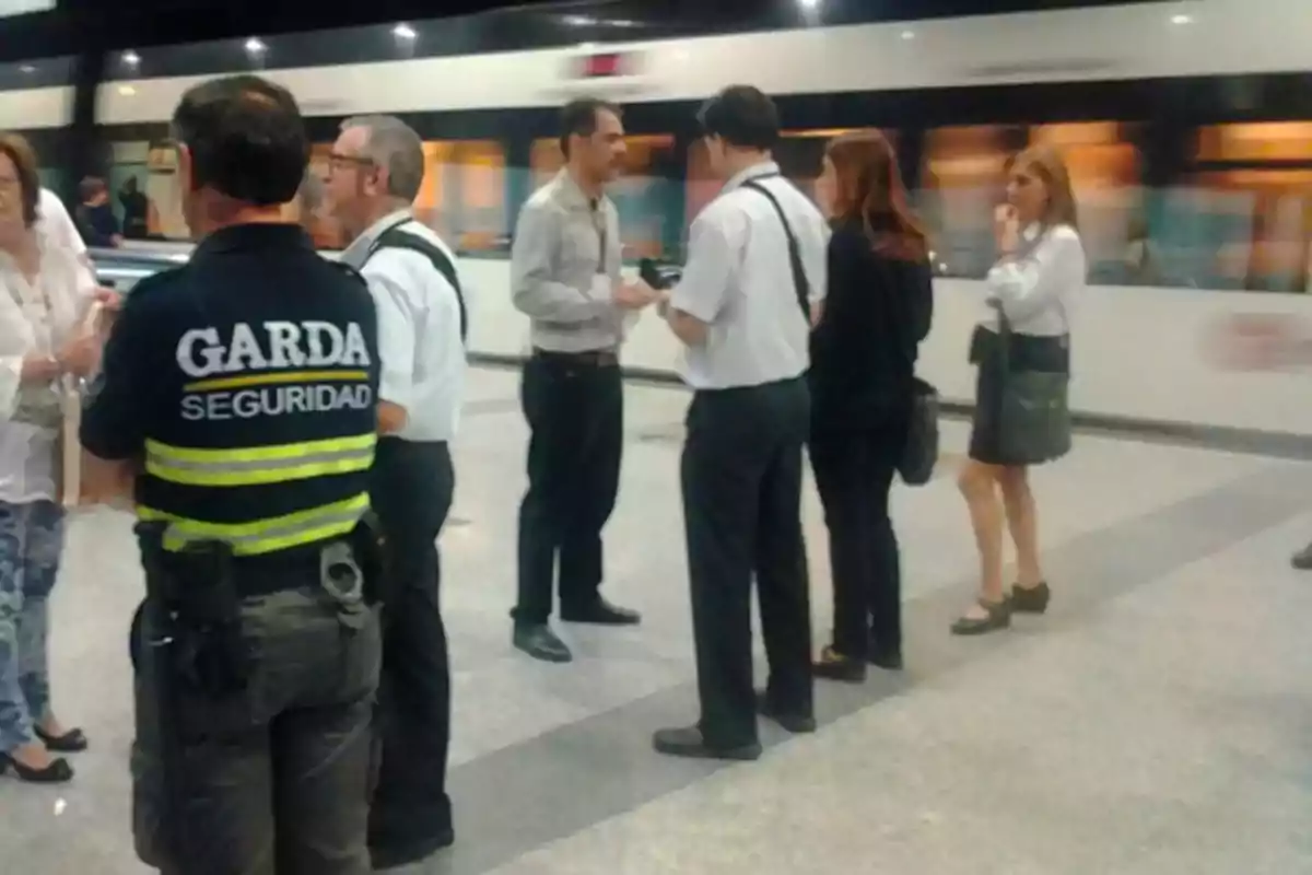 Un grupo de personas, incluyendo un guardia de seguridad, conversan en una estación de tren o metro.