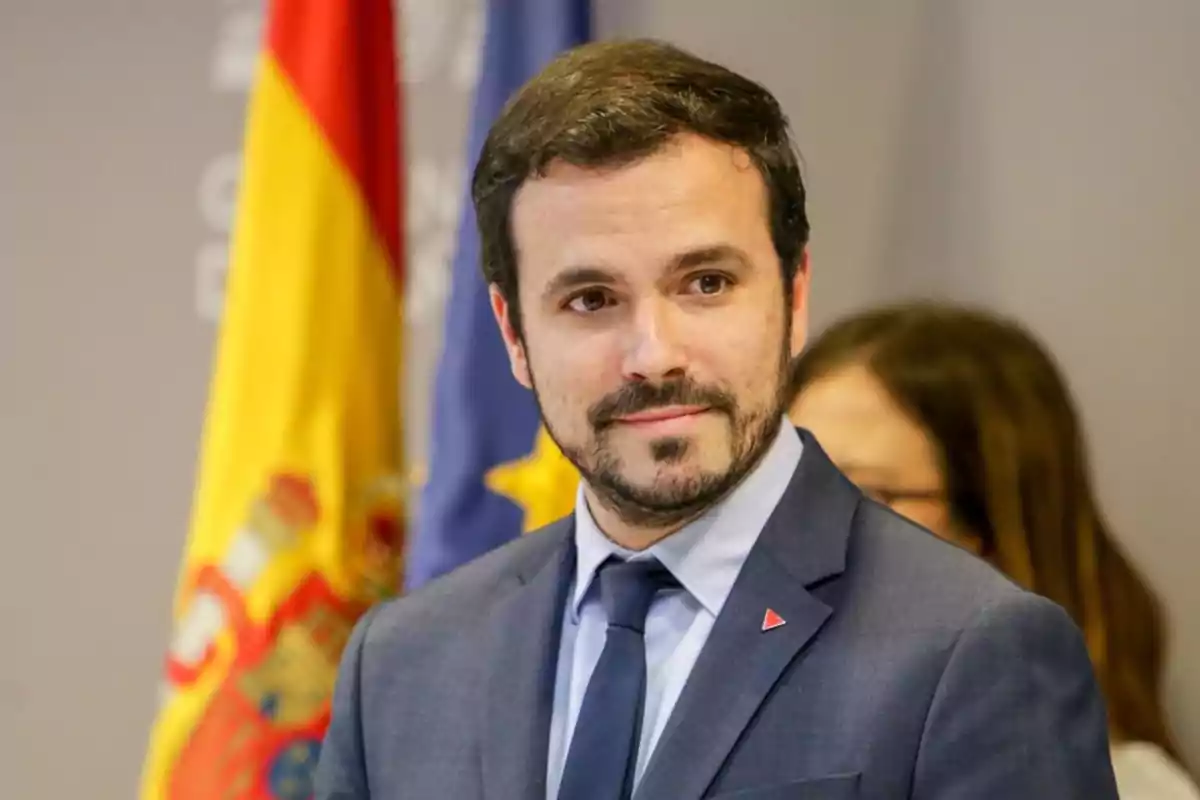 Un hombre con traje y corbata está de pie frente a las banderas de España y la Unión Europea.