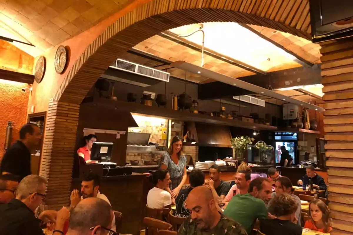 Un grupo de personas disfruta de una comida en un restaurante con un ambiente cálido y acogedor, con techos abovedados y decoración rústica.