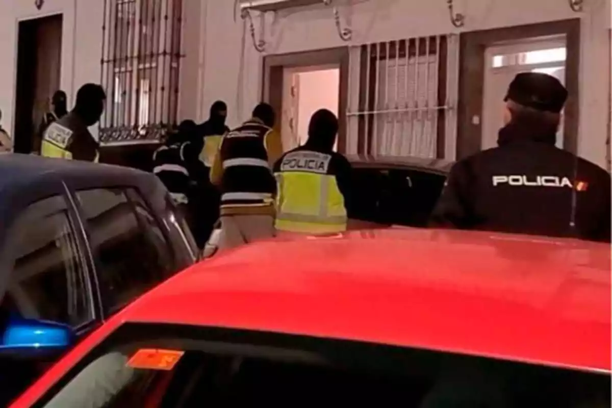 Un grupo de policías realiza una operación en la entrada de un edificio, con varios vehículos estacionados en la calle. Un grupo de policías realiza una operación en la entrada de un edificio, con varios vehículos estacionados en la calle.