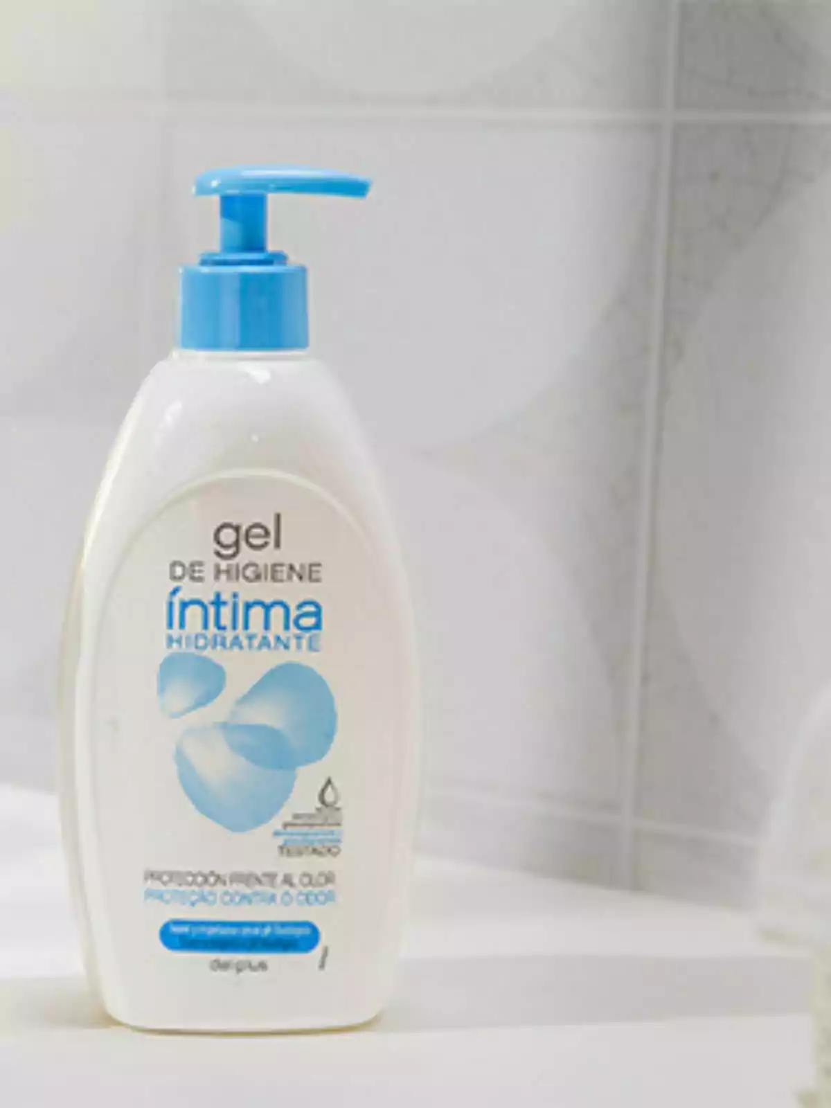 Botella de gel de higiene íntima hidratante con dispensador azul sobre una superficie blanca. Botella de gel de higiene íntima hidratante con dispensador azul sobre una superficie blanca.