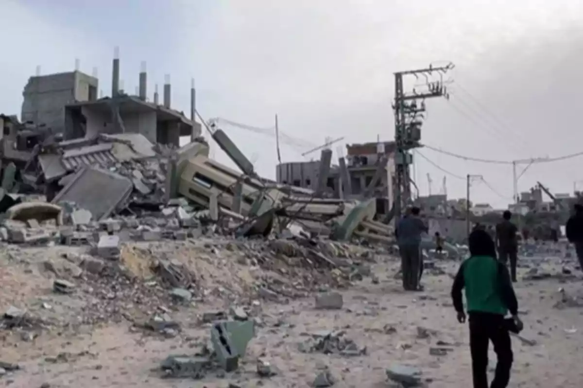 Edificios destruidos y personas caminando entre escombros en una zona afectada por un conflicto Edificios destruidos y personas caminando entre escombros en una zona afectada por un conflicto