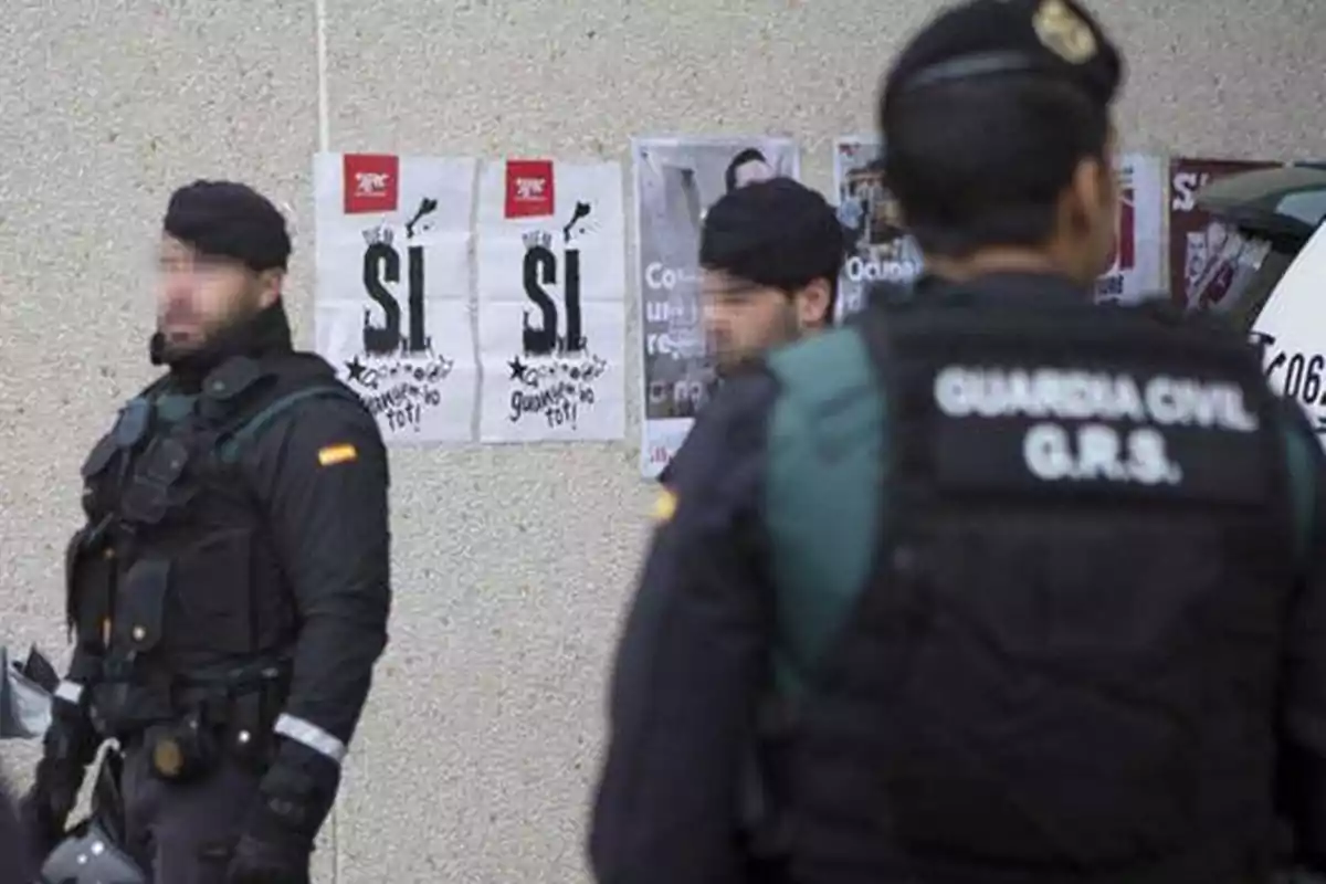 Agentes de la Guardia Civil en uniforme frente a una pared con carteles que dicen Agentes de la Guardia Civil en uniforme frente a una pared con carteles que dicen