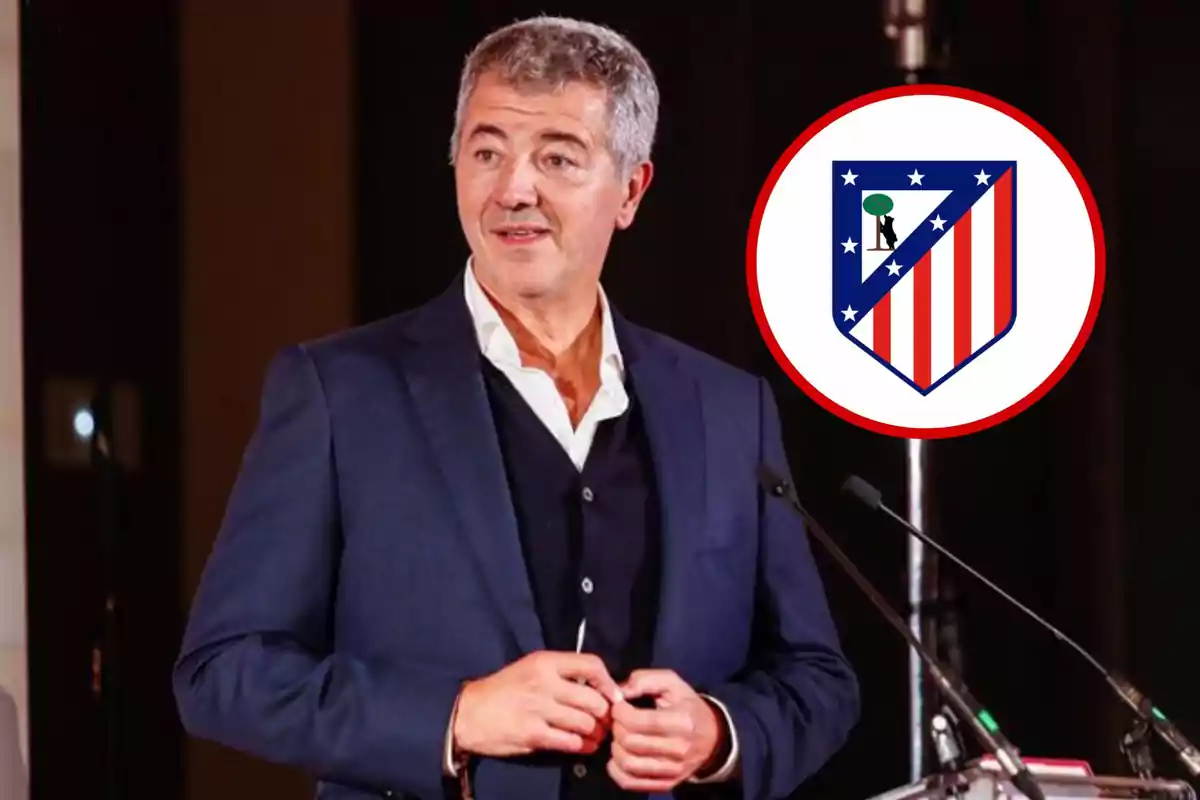 Un hombre en traje oscuro está de pie frente a un micrófono con el escudo del Atlético de Madrid al fondo.