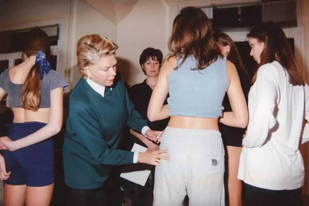 Un grupo de personas en una habitación, con una mujer mayor ajustando la ropa de una joven.