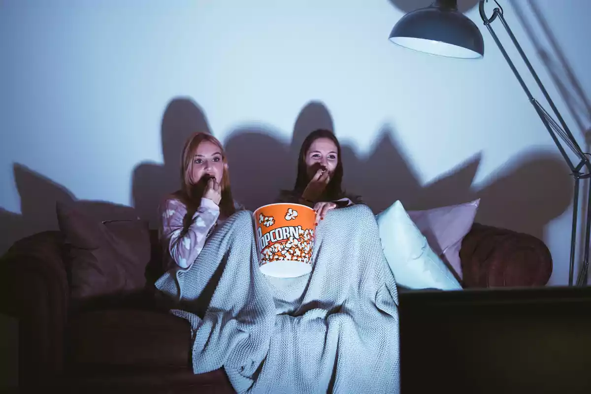 Dos personas sentadas en un sofá viendo una película mientras comen palomitas de maíz.