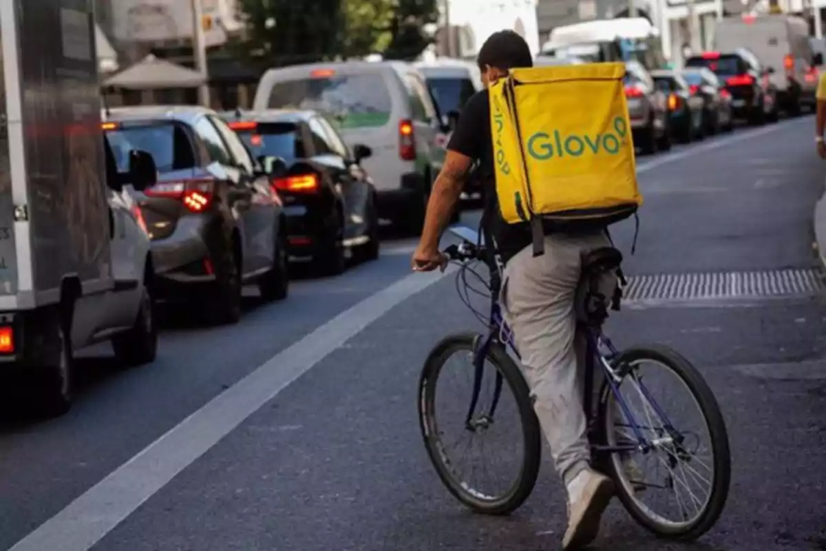 Un repartidor de Glovo en bicicleta circula por una calle con tráfico.