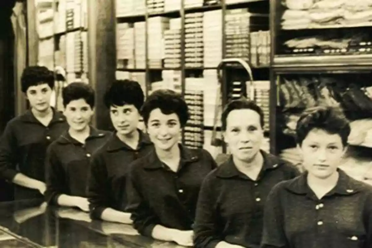 Un grupo de mujeres posando en una tienda antigua, con estanterías llenas de productos en el fondo.