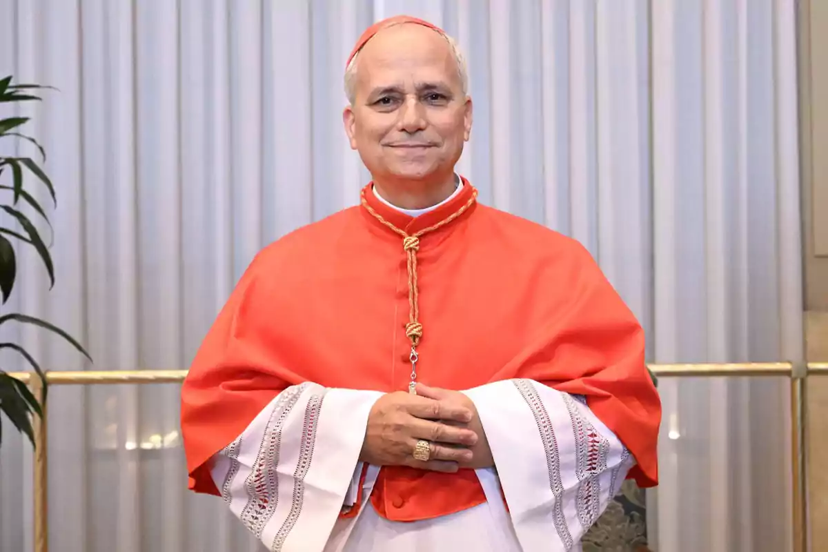Un hombre con vestimenta religiosa roja y blanca, de pie frente a una cortina, con las manos juntas. Un hombre con vestimenta religiosa roja y blanca, de pie frente a una cortina, con las manos juntas.