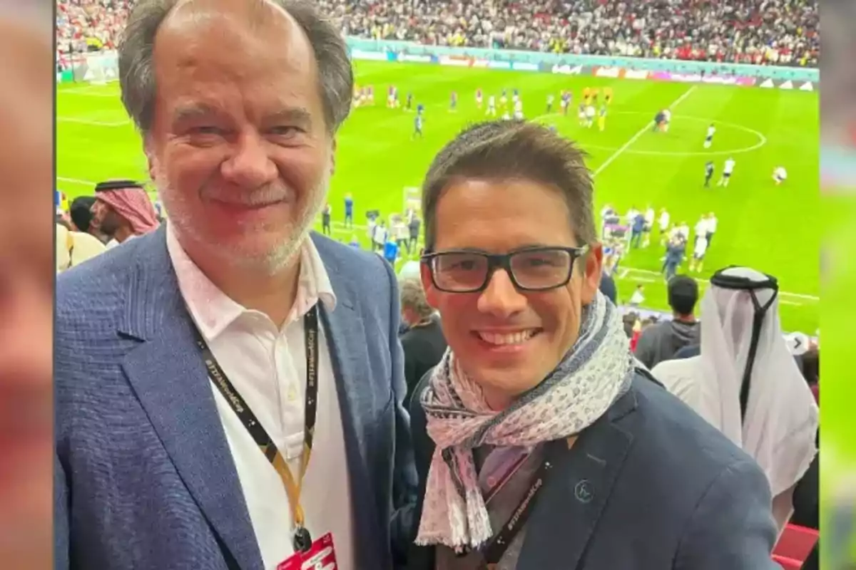 Dos personas sonríen en un estadio de fútbol lleno de espectadores.