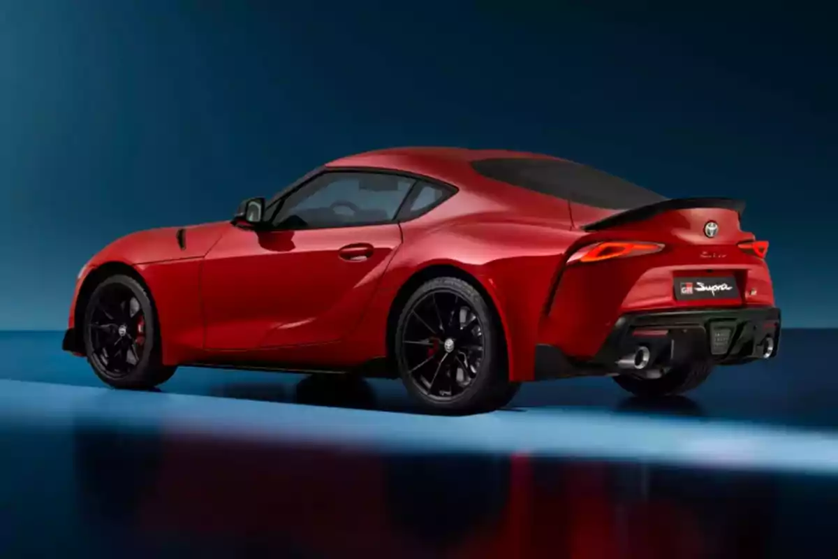 Coche deportivo rojo visto de perfil trasero sobre un fondo azul.