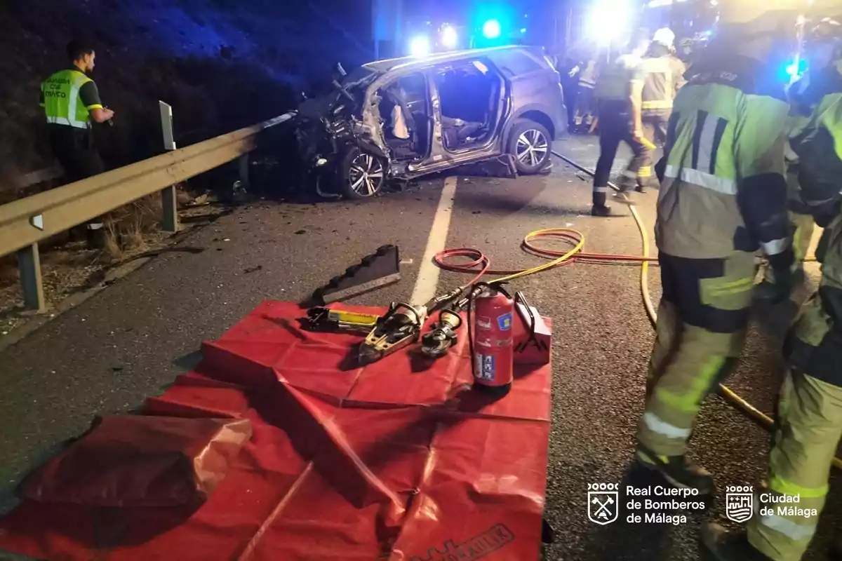 Bomberos y personal de emergencia atienden un accidente de tráfico nocturno en una carretera donde un coche ha chocado contra la valla de protección y se observan herramientas de rescate sobre una lona roja Bomberos y personal de emergencia atienden un accidente de tráfico nocturno en una carretera donde un coche ha chocado contra la valla de protección y se observan herramientas de rescate sobre una lona roja