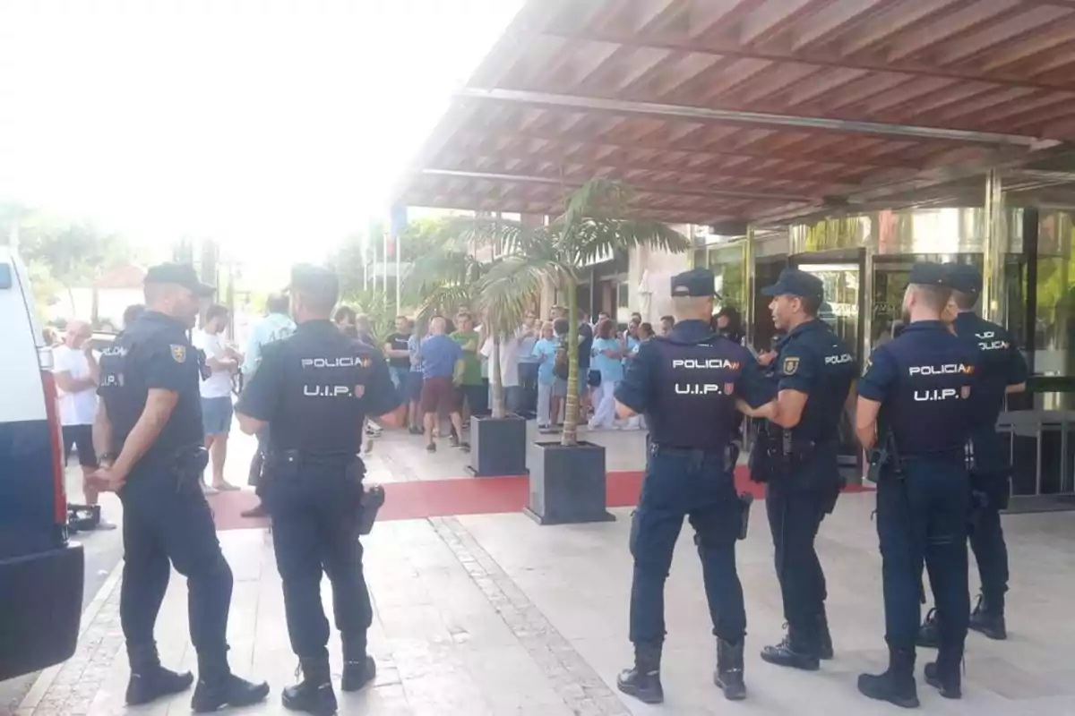 Policías de la UIP vigilando una entrada mientras un grupo de personas se reúne en el fondo.