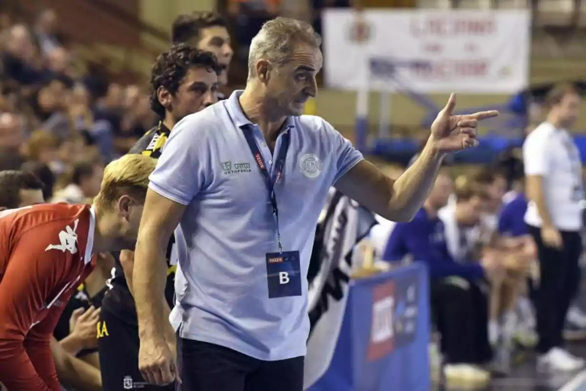 Entrenador de balonmano dando indicaciones a su equipo durante un partido en un pabellón deportivo lleno de espectadores Entrenador de balonmano dando indicaciones a su equipo durante un partido en un pabellón deportivo lleno de espectadores
