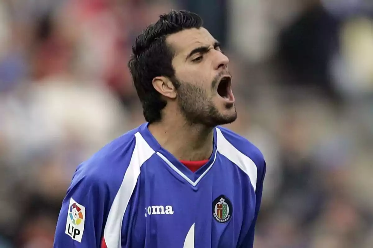 Un jugador de fútbol con uniforme azul grita durante un partido.