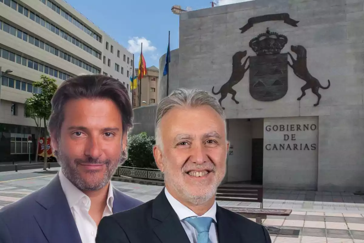 Dos hombres posan frente al edificio del Gobierno de Canarias con el escudo y banderas en el fondo.
