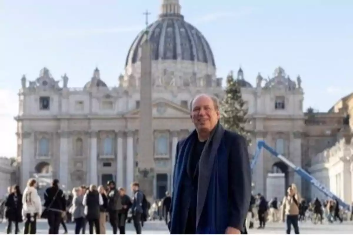 Un hombre sonriente frente a la Basílica de San Pedro en el Vaticano con varias personas alrededor.