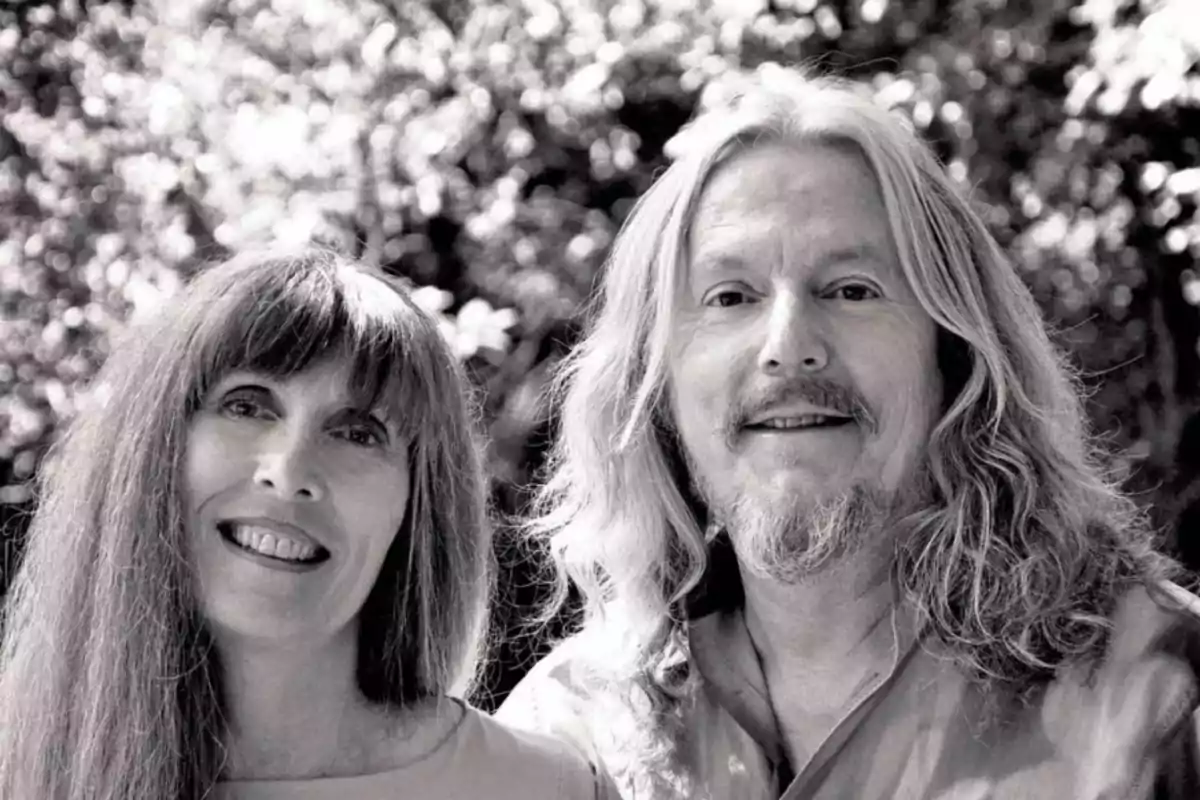 Una pareja sonriente con cabello largo y suelto, posando al aire libre con un fondo de vegetación.