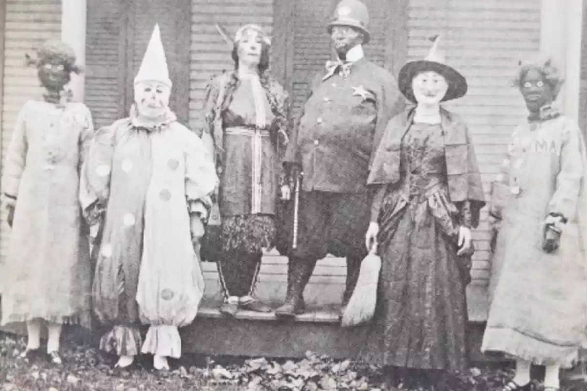 Un grupo de personas disfrazadas posando frente a una casa en una fotografía antigua.