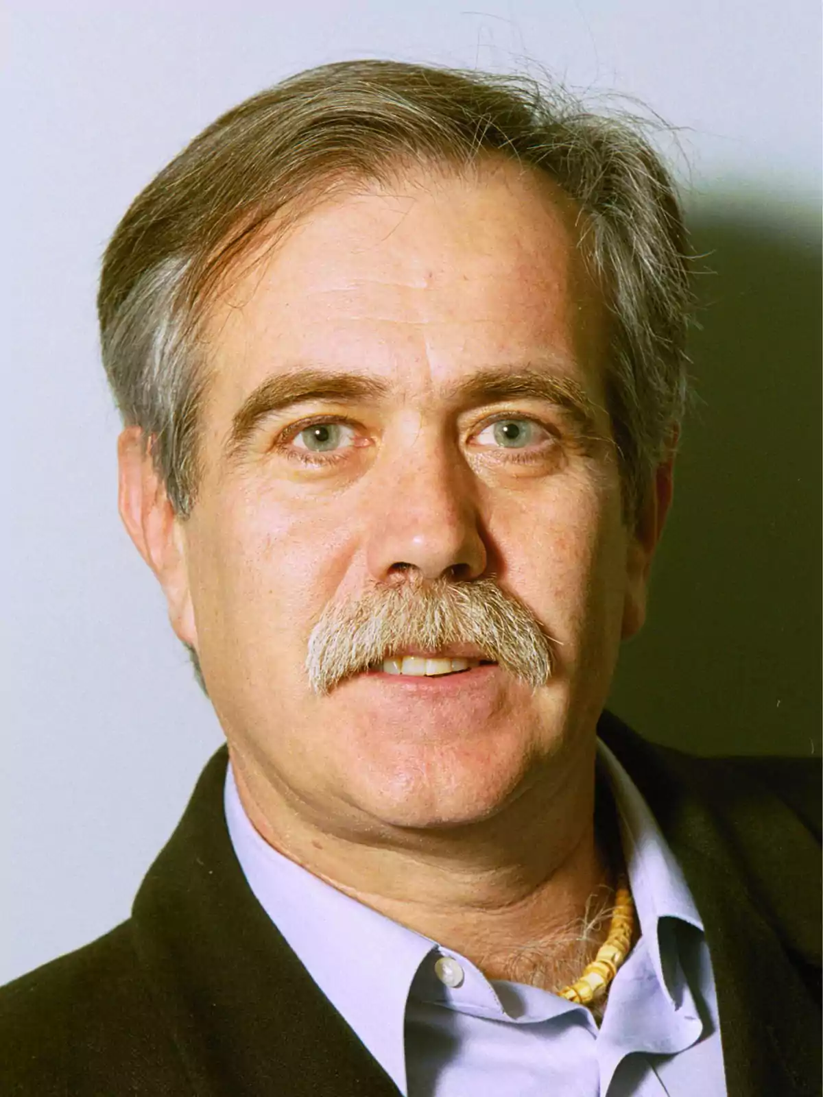 Un hombre de mediana edad con cabello canoso y bigote, vistiendo una camisa azul y chaqueta oscura, mirando a la cámara.