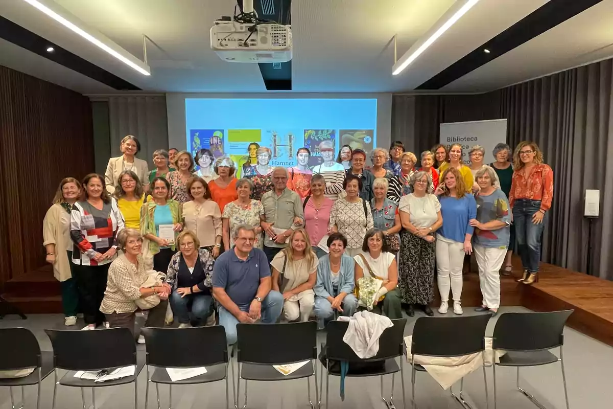 Un grupo de personas posando para una foto en una sala con sillas y una pantalla de proyección al fondo.